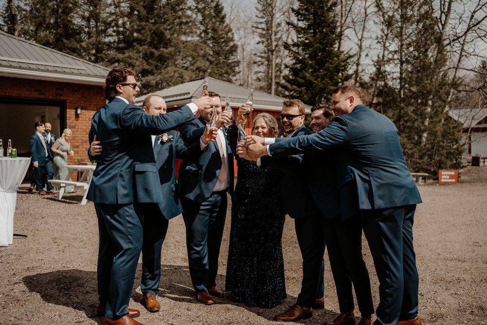 Wedding party in navy blue suits standing together in close formation for a candid group shot outdoors.