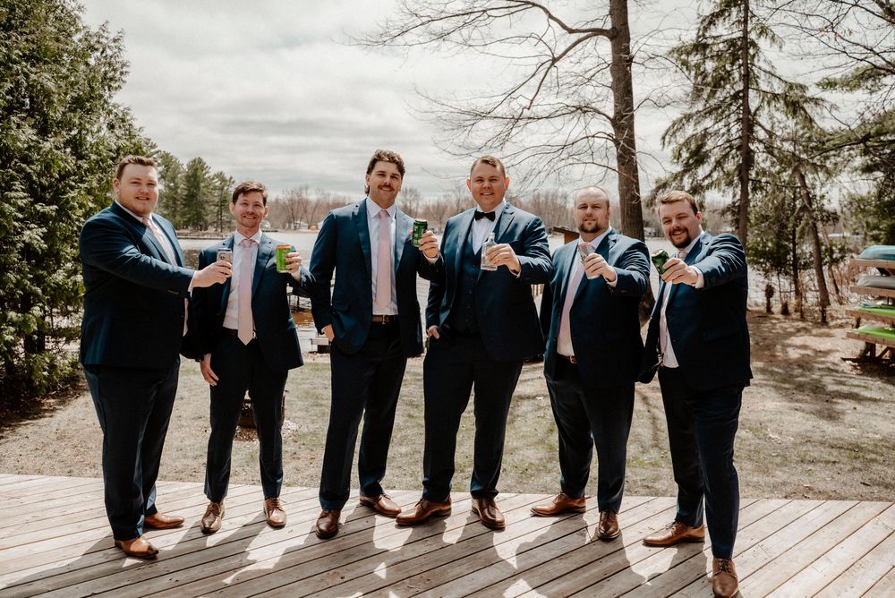 Wedding party wearing black tuxedos and blue bowties show off their colorful socks while posing on a wooden deck.