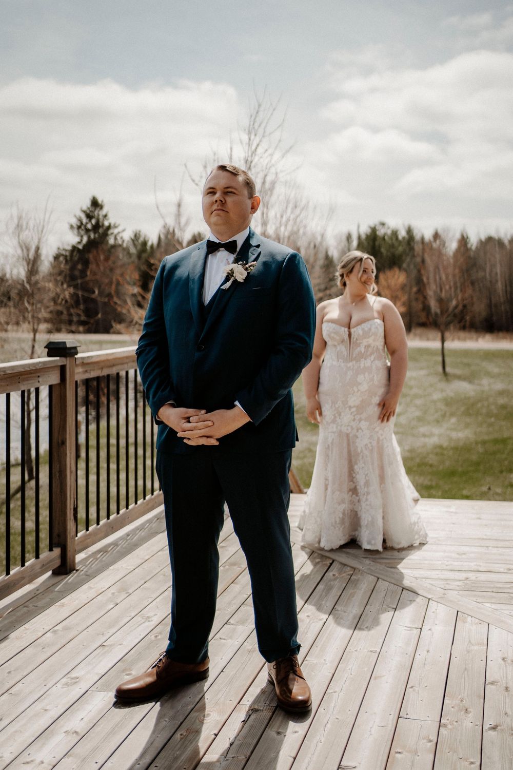 A wedding couple stands on a wooden deck with mountain views during their first look.