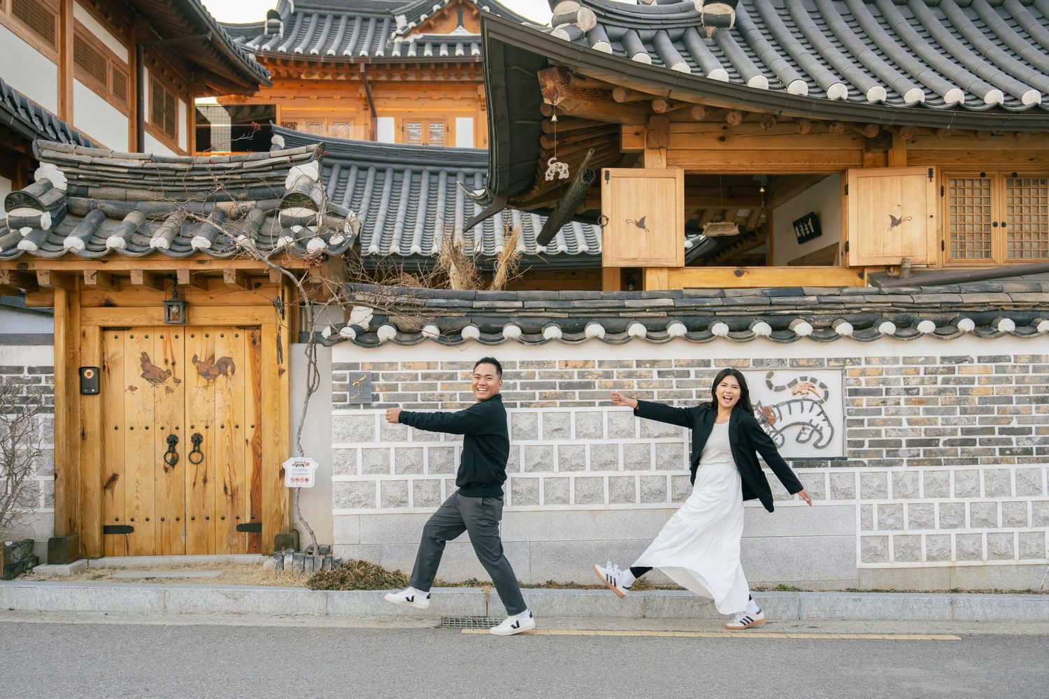 Couple strolling hand in hand through traditional Korean hanok village courtyard with ornate wooden buildings.