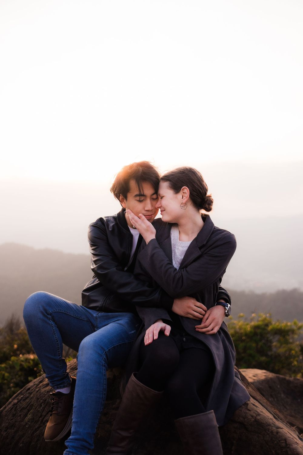 A romantic couple embrace while sitting on rocks during a misty sunset at Thumb Lookout Mountain.