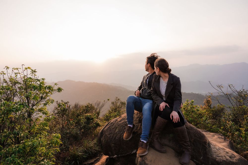 A newly engaged couple look into the distance at the Taipei valley while sitting on a rock at Thumb Lookout Mountain.