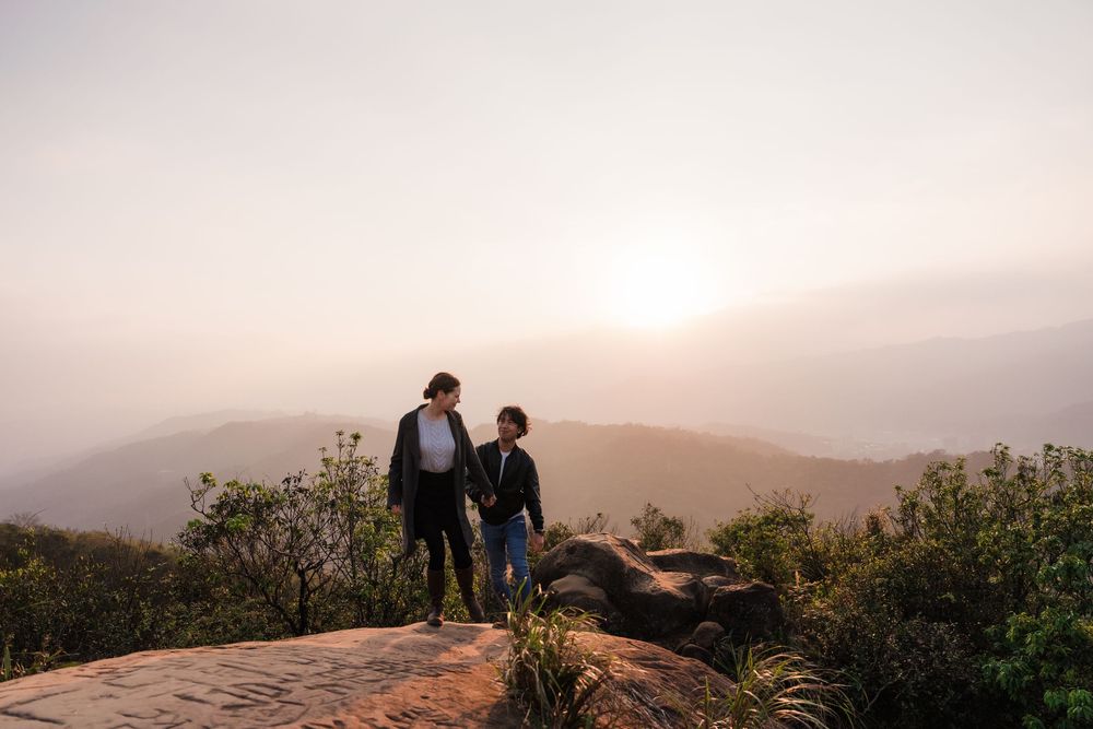 A couple in the distance walks hand in hand over hilltop rocks at Thumb Lookout Mountain Taipei during a misty sunset.