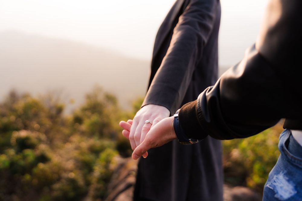 Artistic style close up of a couple holding hands displaying an engagement ring in a warm natural setting at sunset