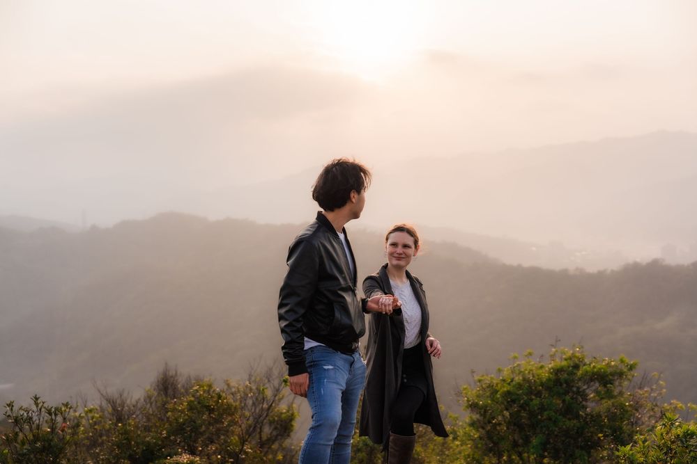 A couple holding hands enjoying a scenic Taipei mountain overlook at sunset with fog rolling through the hills in the background.