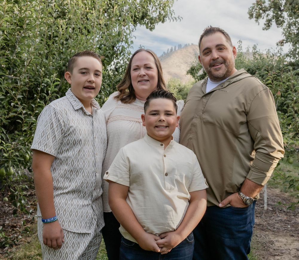 Family members pose together outdoors among trees on a bright day.