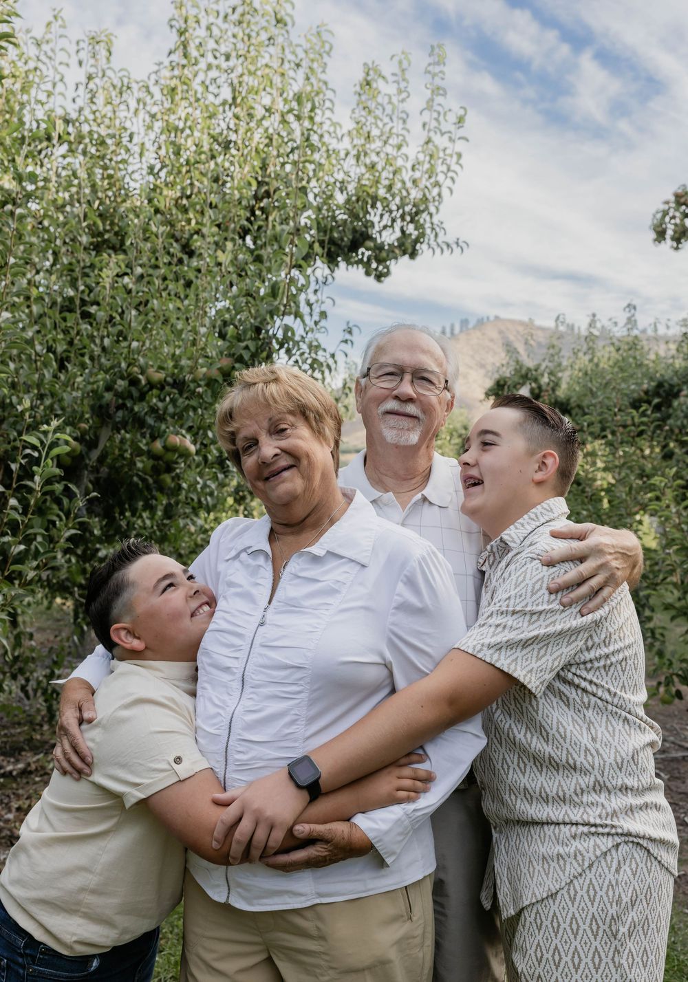 Multi-generational family sharing playful moments and laughter in an orchard setting.