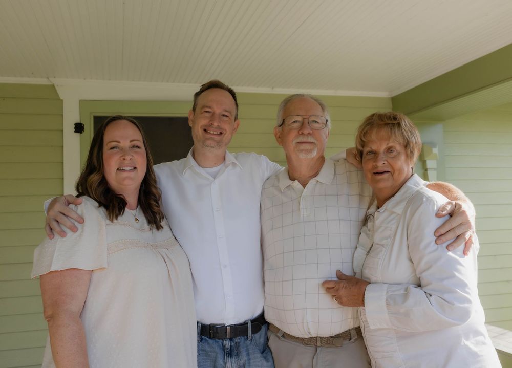 Family group poses together on a porch wearing coordinated white and light-colored outfits.