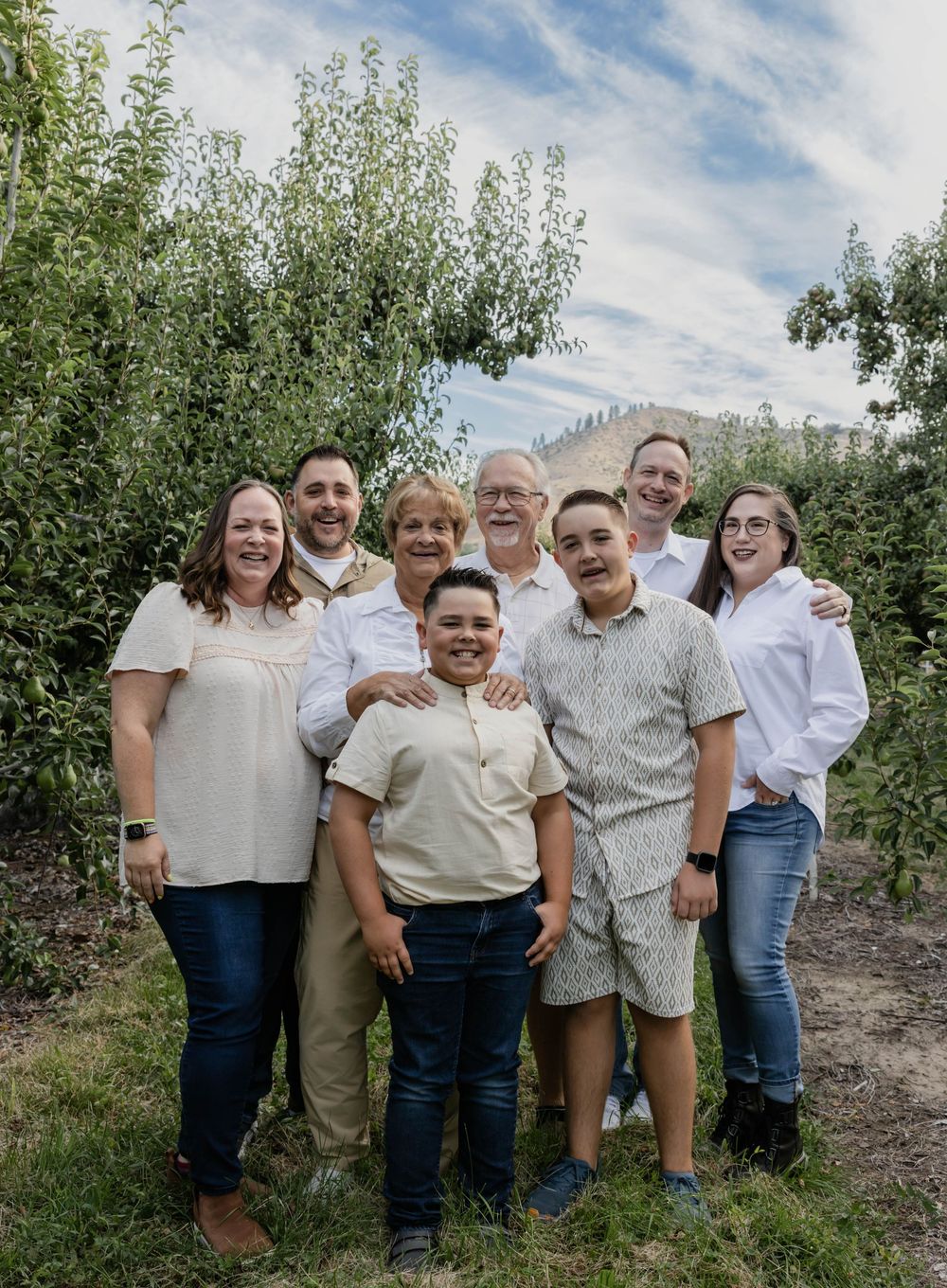 Extended family gathering outdoors for casual group photos in an orchard setting.