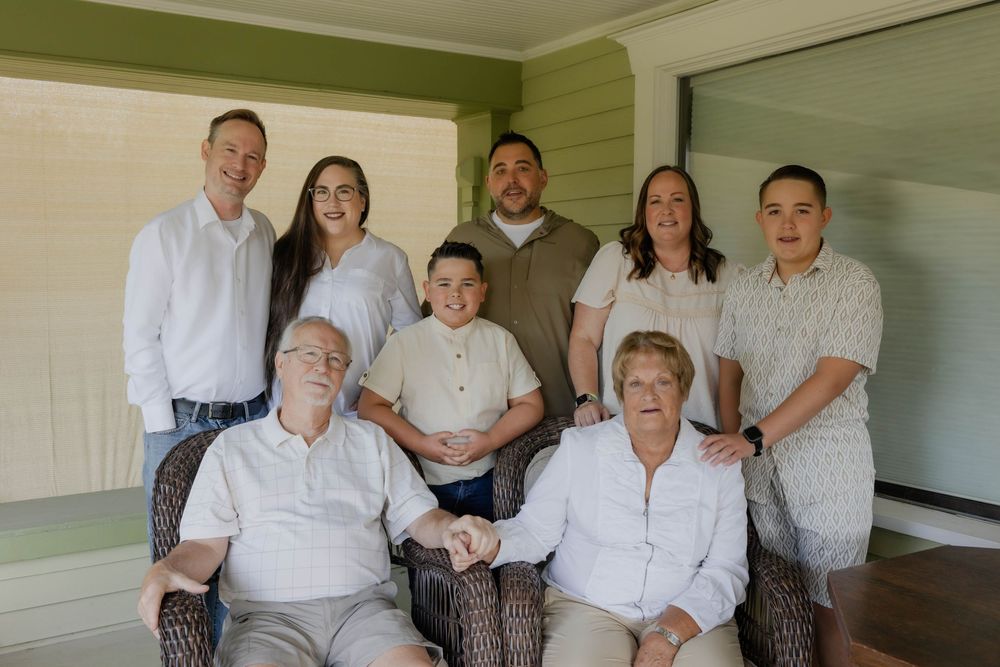 Family photo session on a front porch with coordinated white and gray outfits.