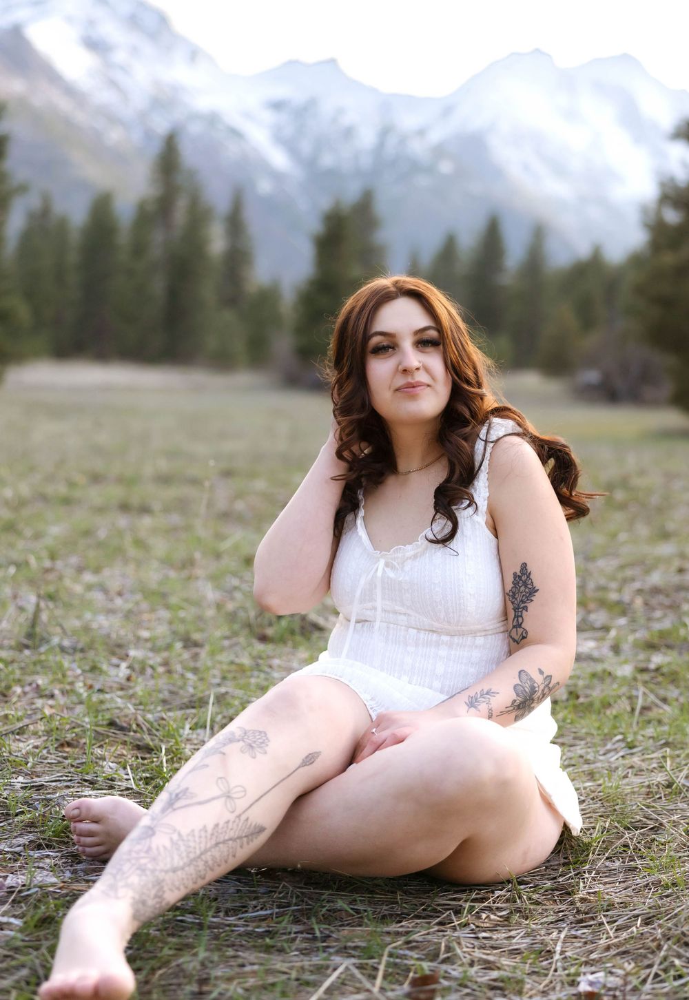 White dress contrasts with mountain meadow and snow-capped peaks in background.