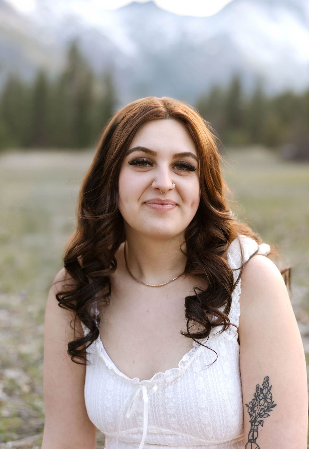 Outdoor portrait with mountains and evergreens in background wearing white dress and delicate necklace.