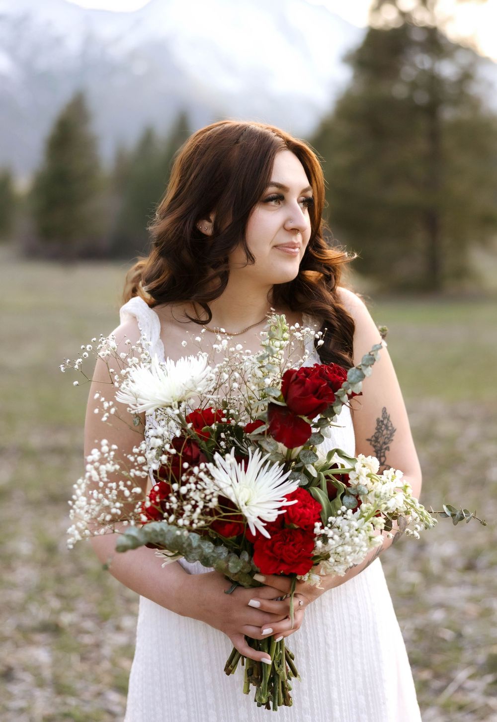Holding bouquet of red roses and white flowers with mountain landscape backdrop.