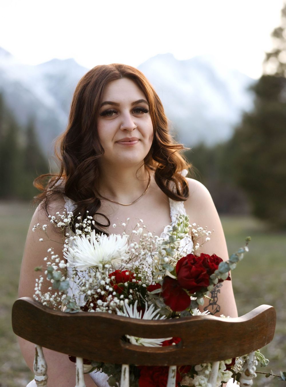 Portrait with red and white floral bouquet against mountain scenery.