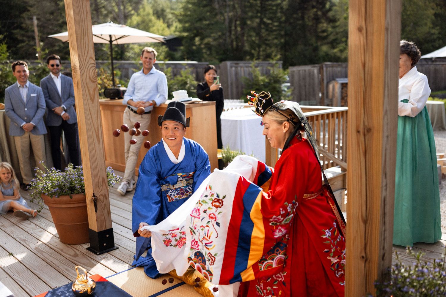 Wedding guests and participants gather for a traditional Korean ceremony in a garden setting.