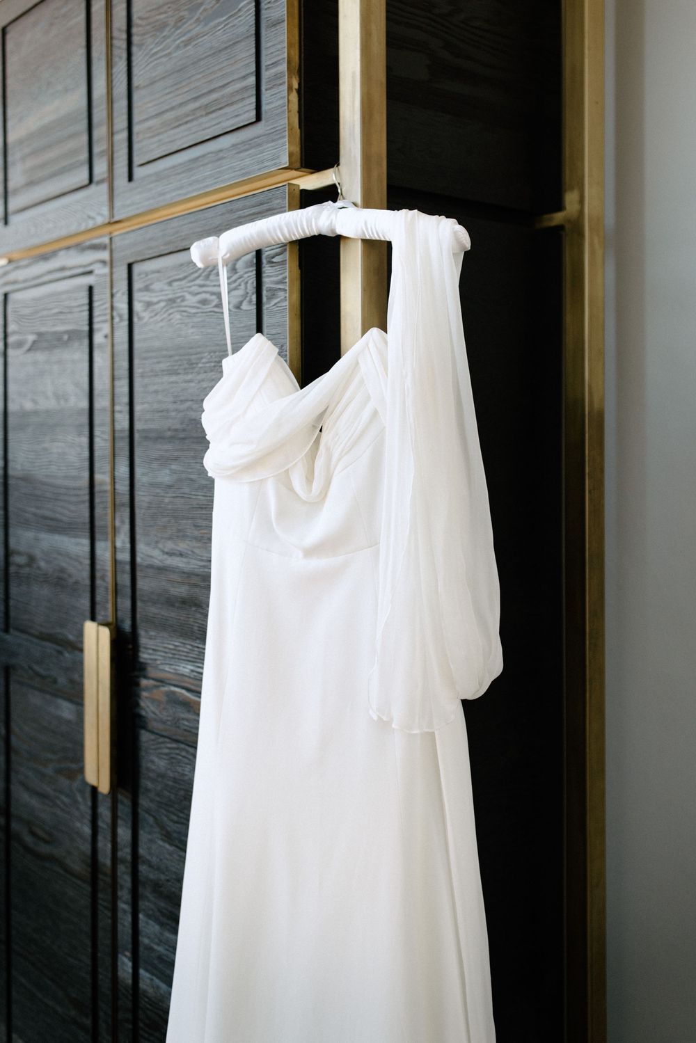 White wedding dresses hanging on gold hangers against a marble wall.