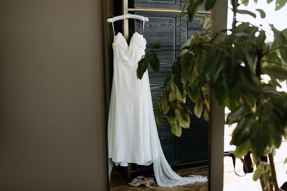 Elegant white wedding gown displayed against a neutral wall with green foliage.