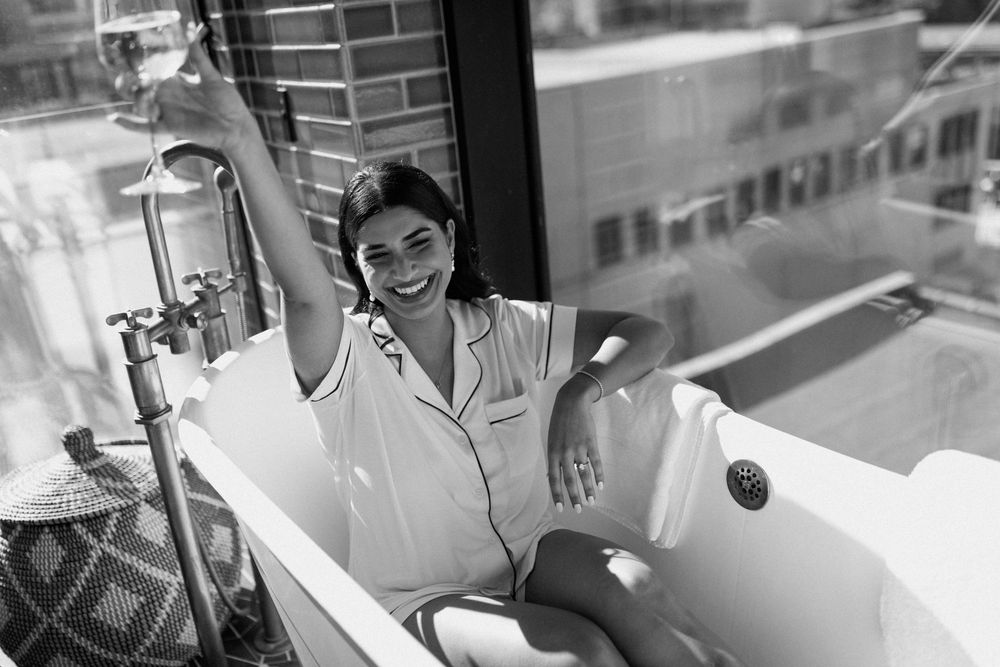 Black and white photo of a bathtub scene with city buildings visible through window.