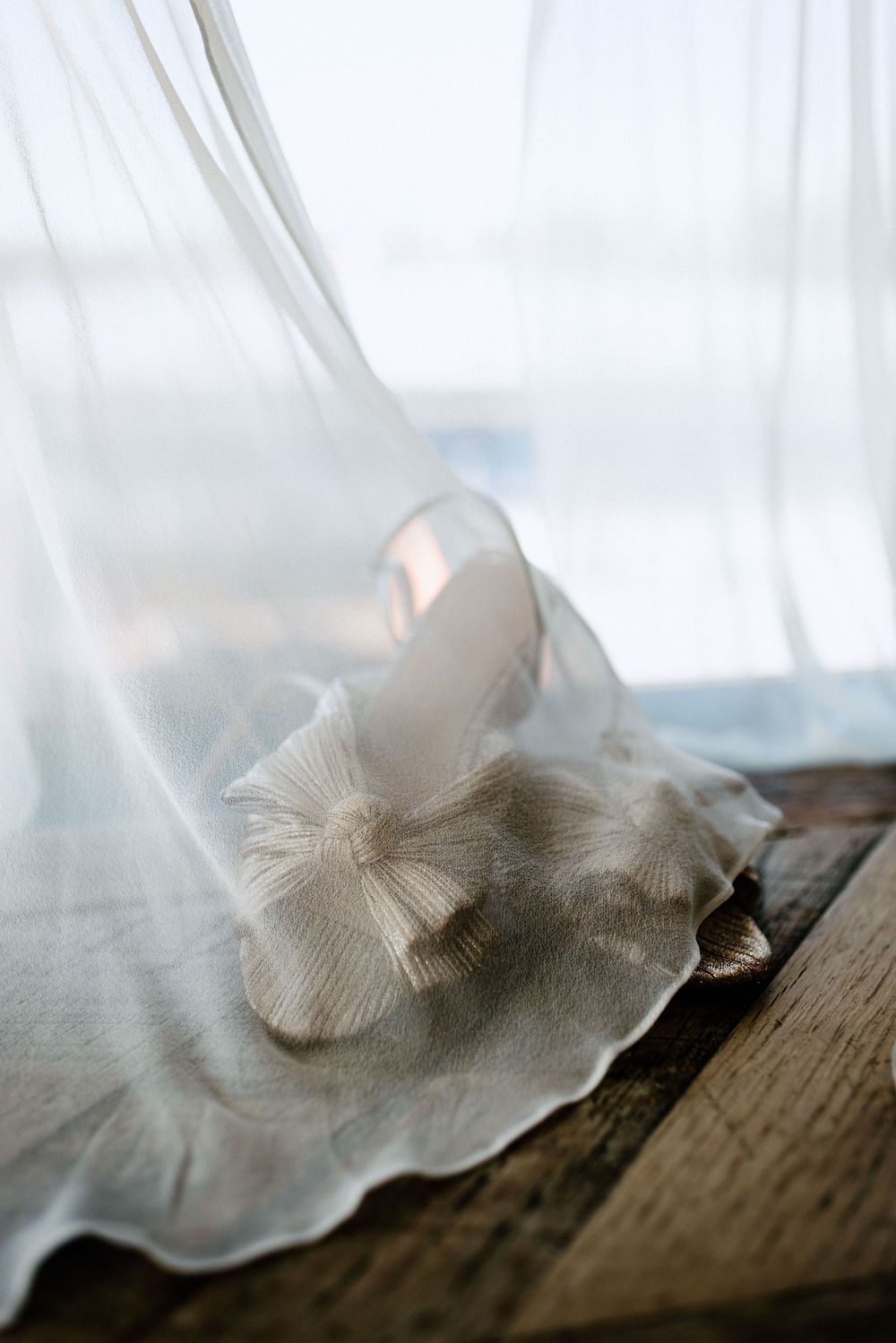 Sheer white curtain detail with wooden floor in soft focus.