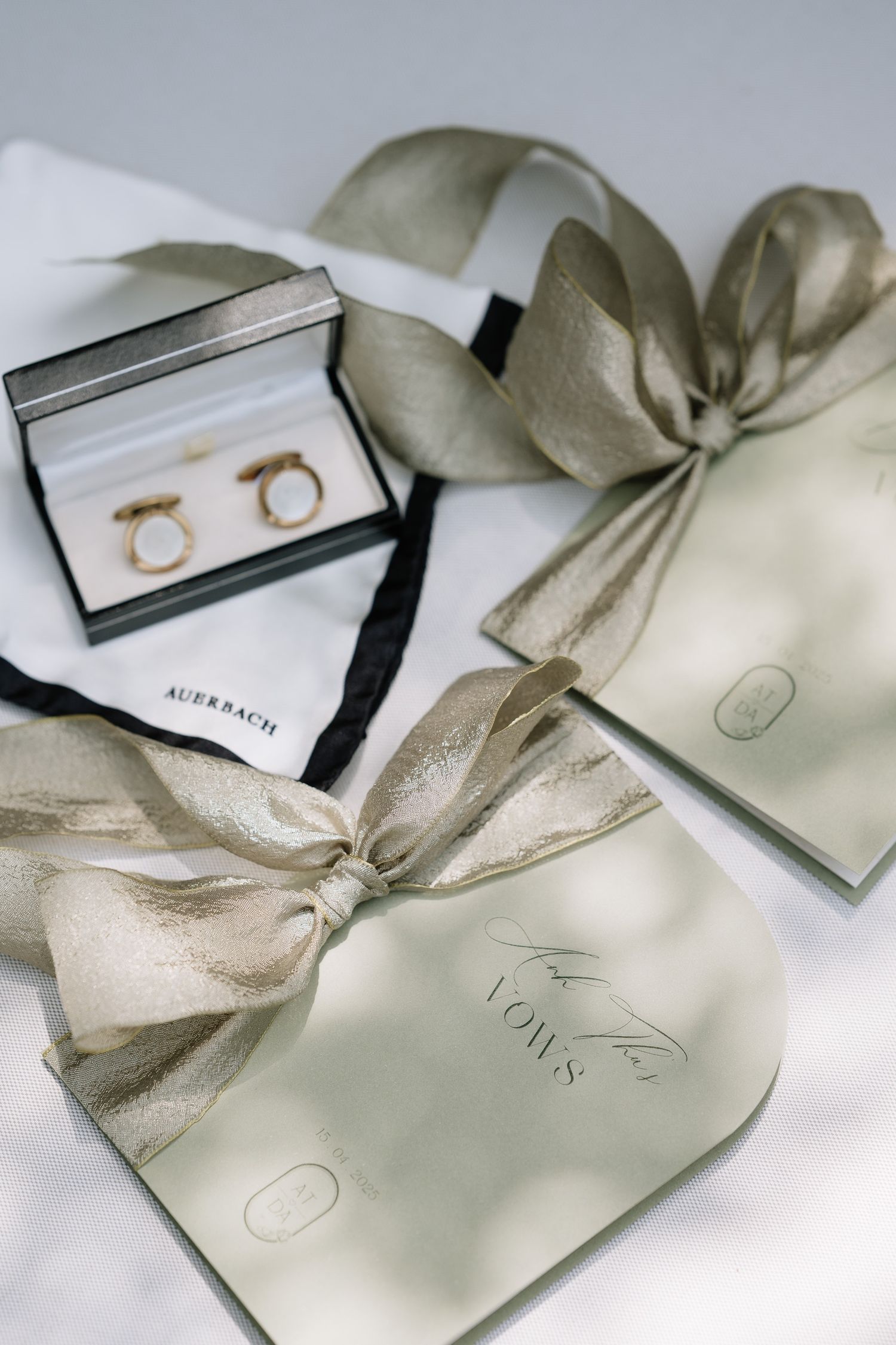 Elegant wedding flat lay with gold rings, sage green vow books, and satin ribbon bows.