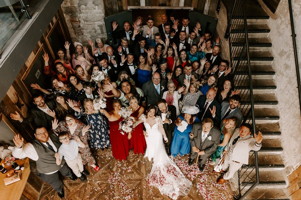 Large crowd of wedding guests gathered on grand staircase throwing petals and confetti in celebration.