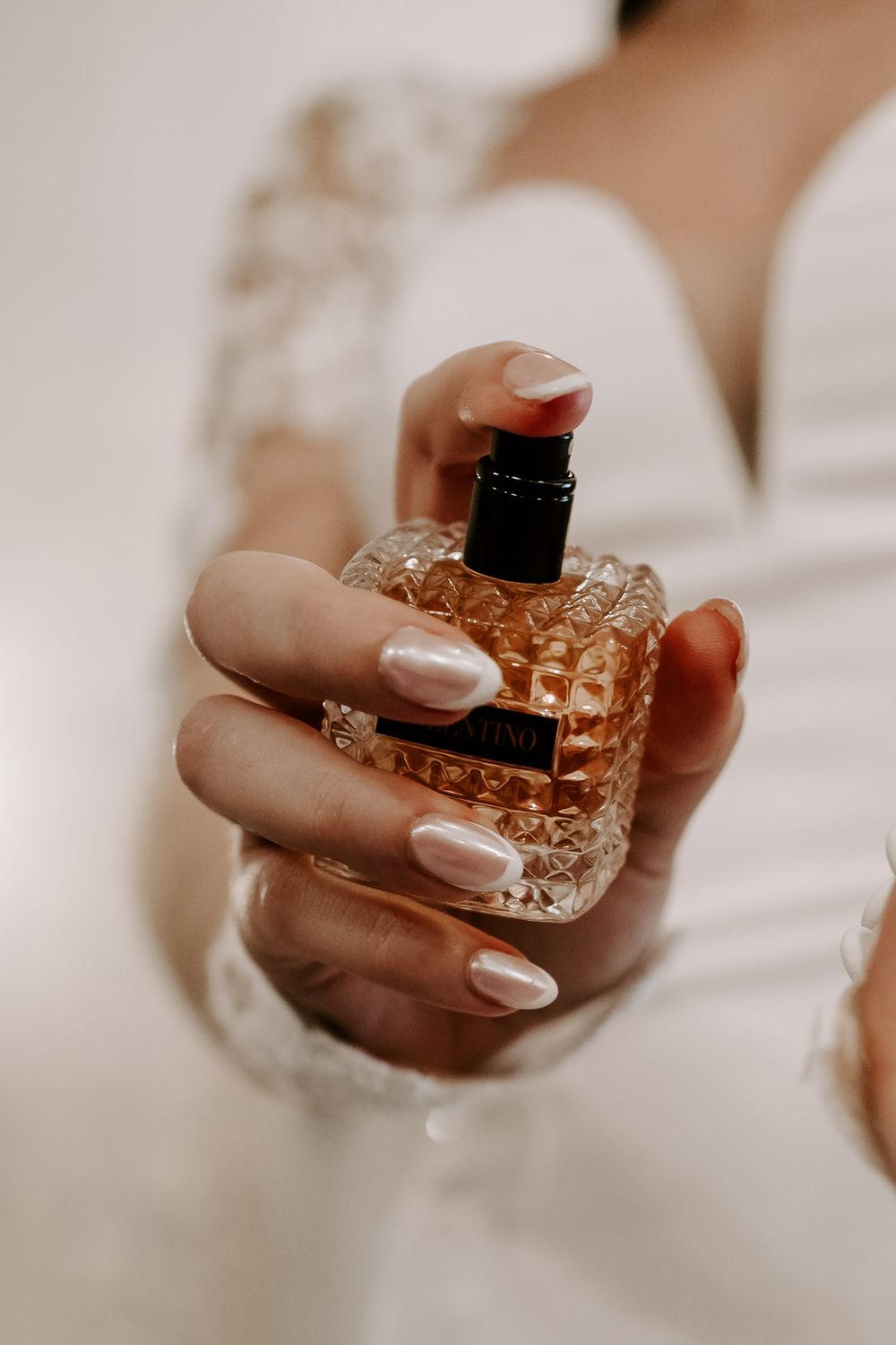 Close-up of hands holding ornate crystal perfume bottle with soft pink manicured nails.