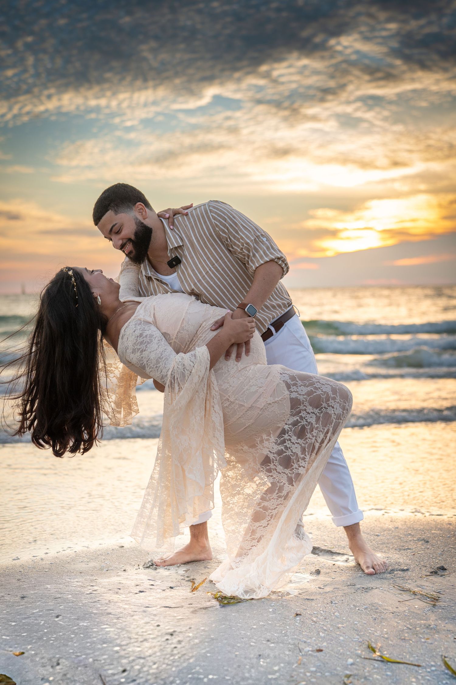 A romantic beach photoshoot with white lace dress and yellow sunset over ocean in the background.