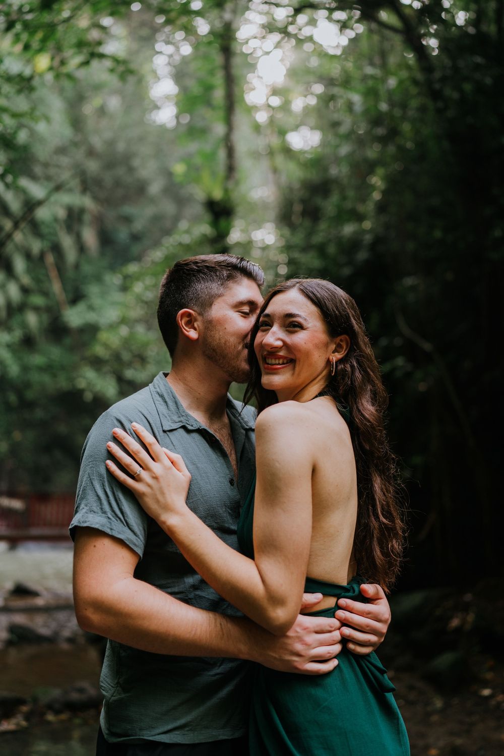 A joyful couple shares a playful moment in a forest setting.