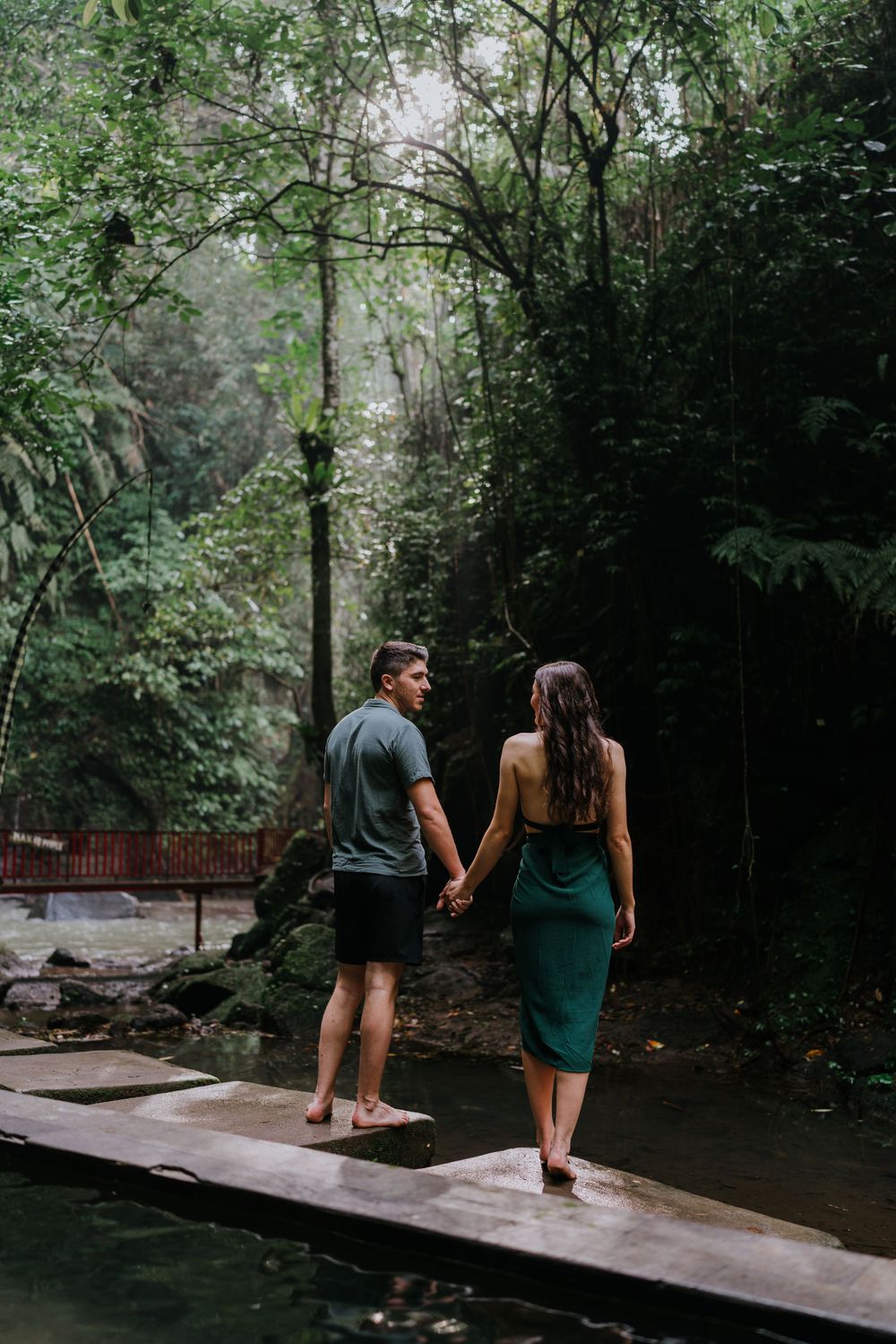Couple walking together on a wooden boardwalk surrounded by dense forest vegetation.