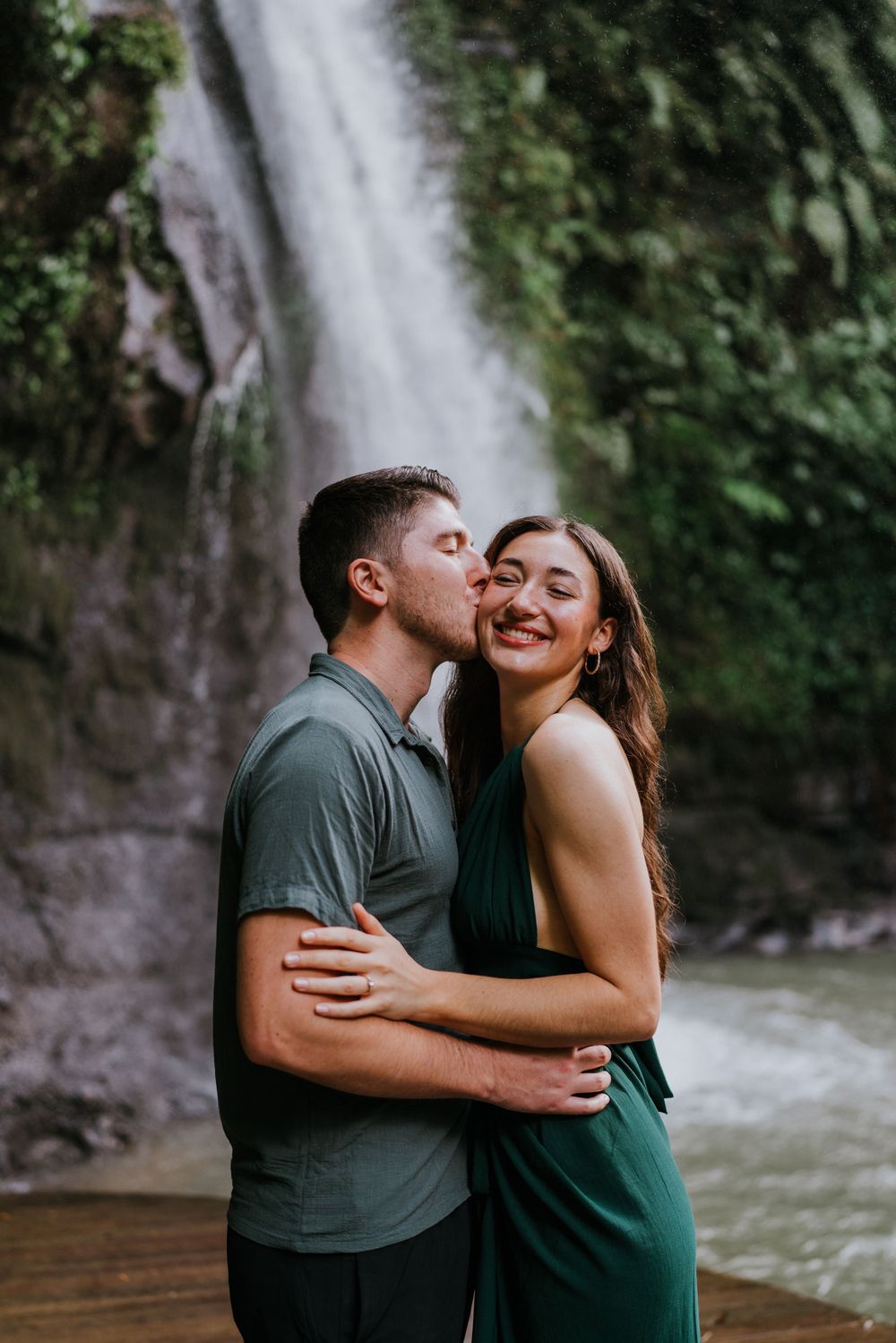 Couple sharing tender moments against a scenic waterfall backdrop in coordinated green outfits.