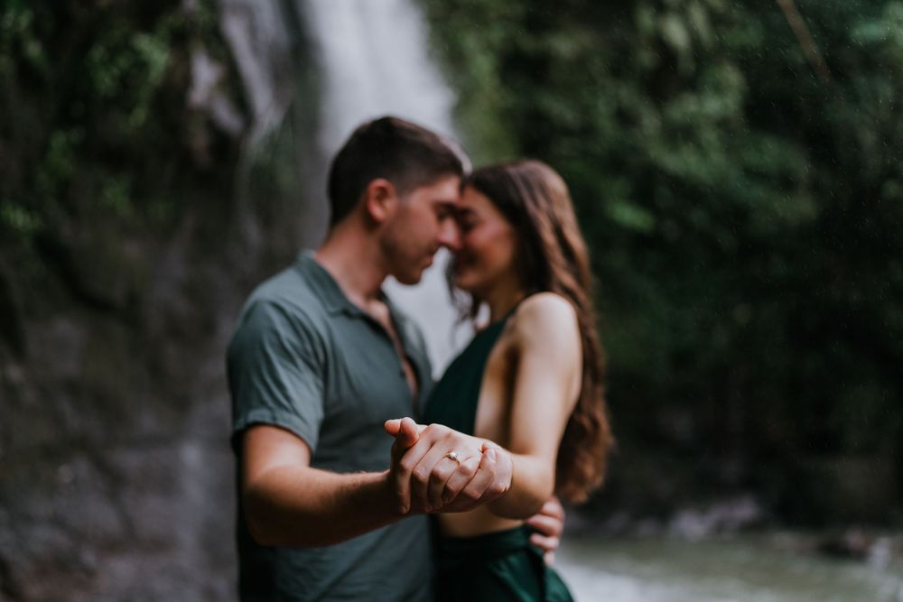 Romantic couple embracing near a waterfall with soft natural lighting.