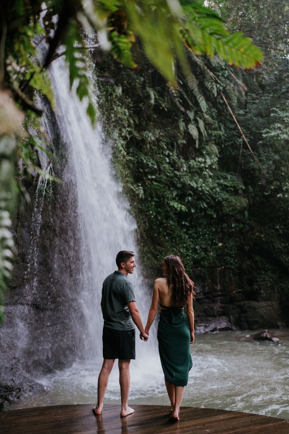 Couple holding hands while walking barefoot near a cascading waterfall.