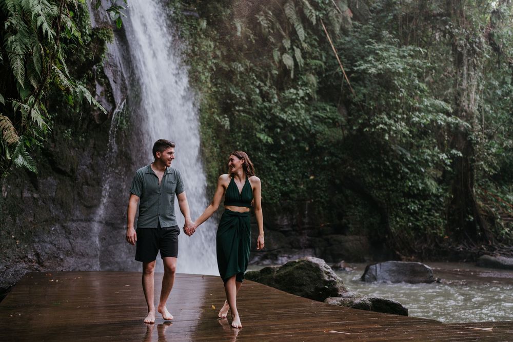 Couple enjoying a peaceful moment by a waterfall on a wooden platform.