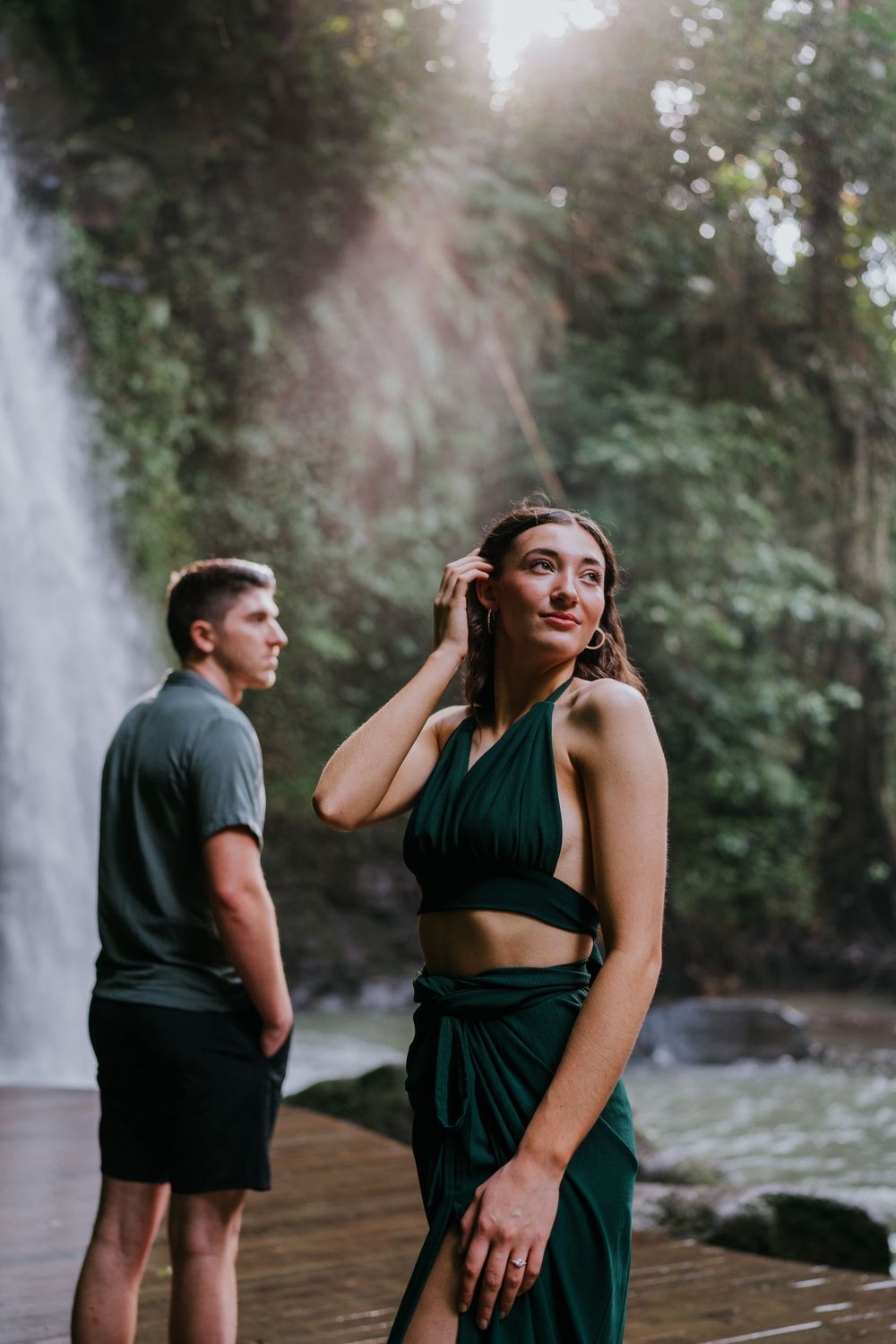 A romantic scene unfolds on a wooden deck with a cascading waterfall in the background.