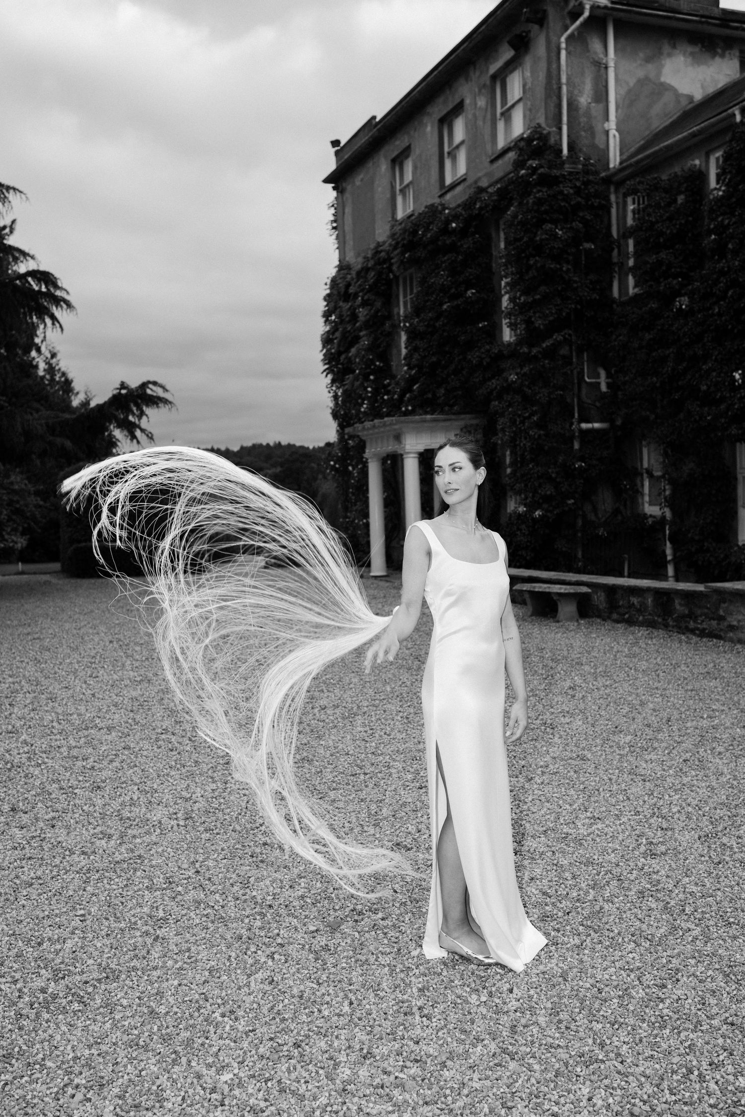 A dramatic black and white photo of a flowing white dress against a historic ivy-covered mansion backdrop.