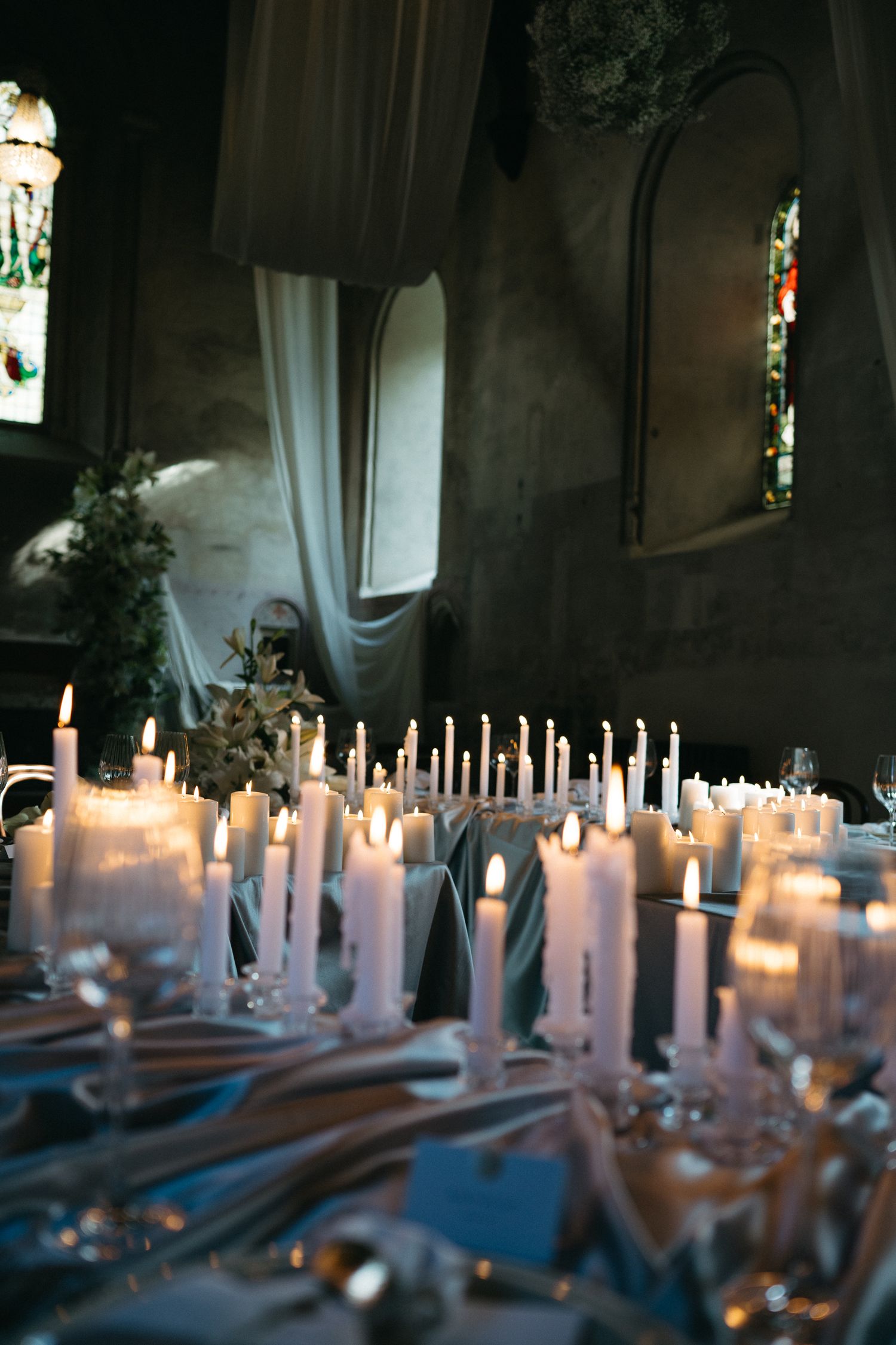 White candles line an elegant table setting with a blue tablecloth at dusk creating a romantic ambiance.