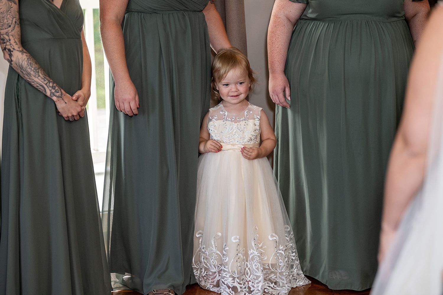 Bridesmaids in elegant forest green gowns stand beside a young flower girl in a white lace dress.