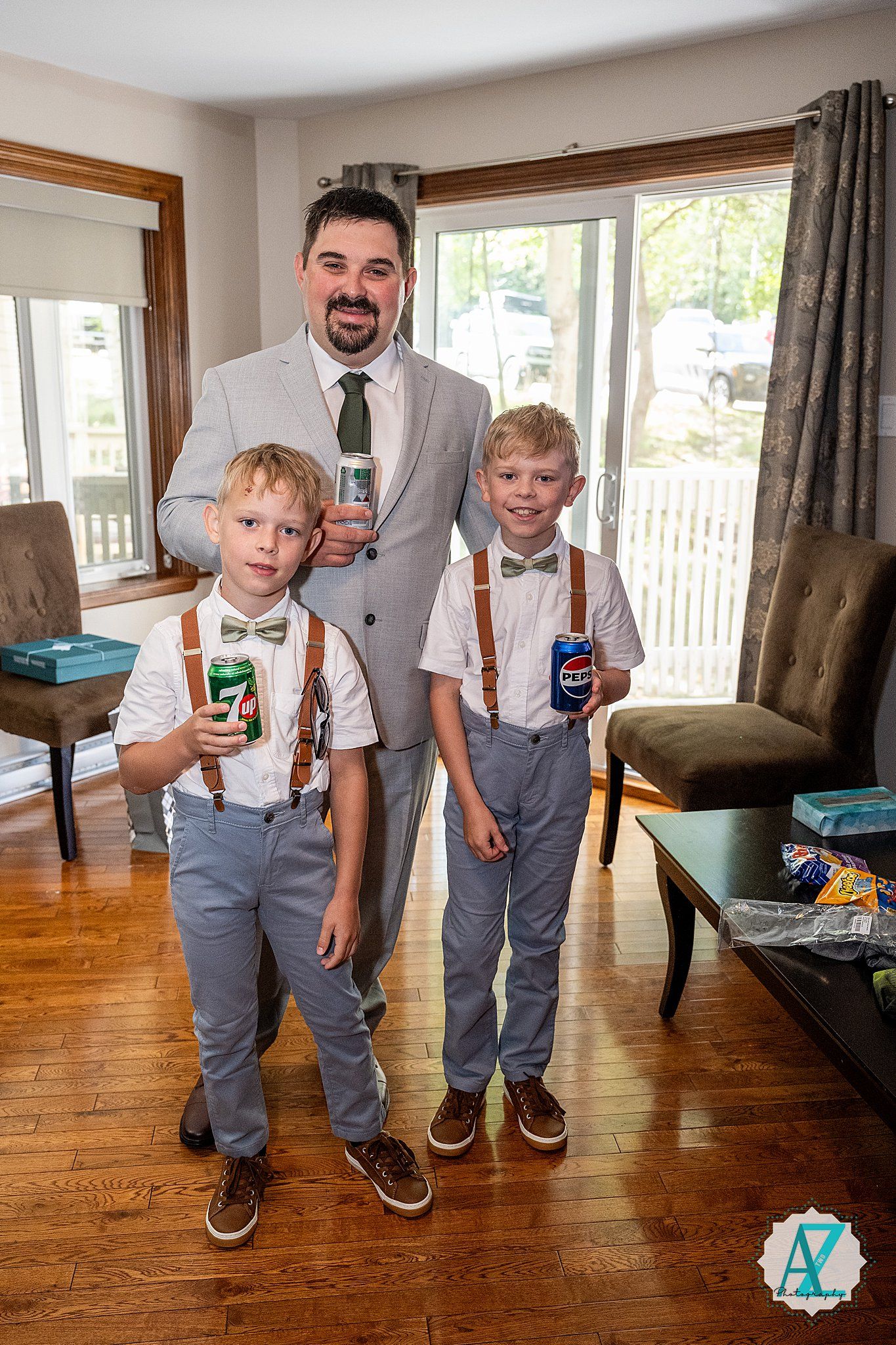 Playful scene with two young people wearing matching gray pants and suspenders against a wooden floor and home interior.