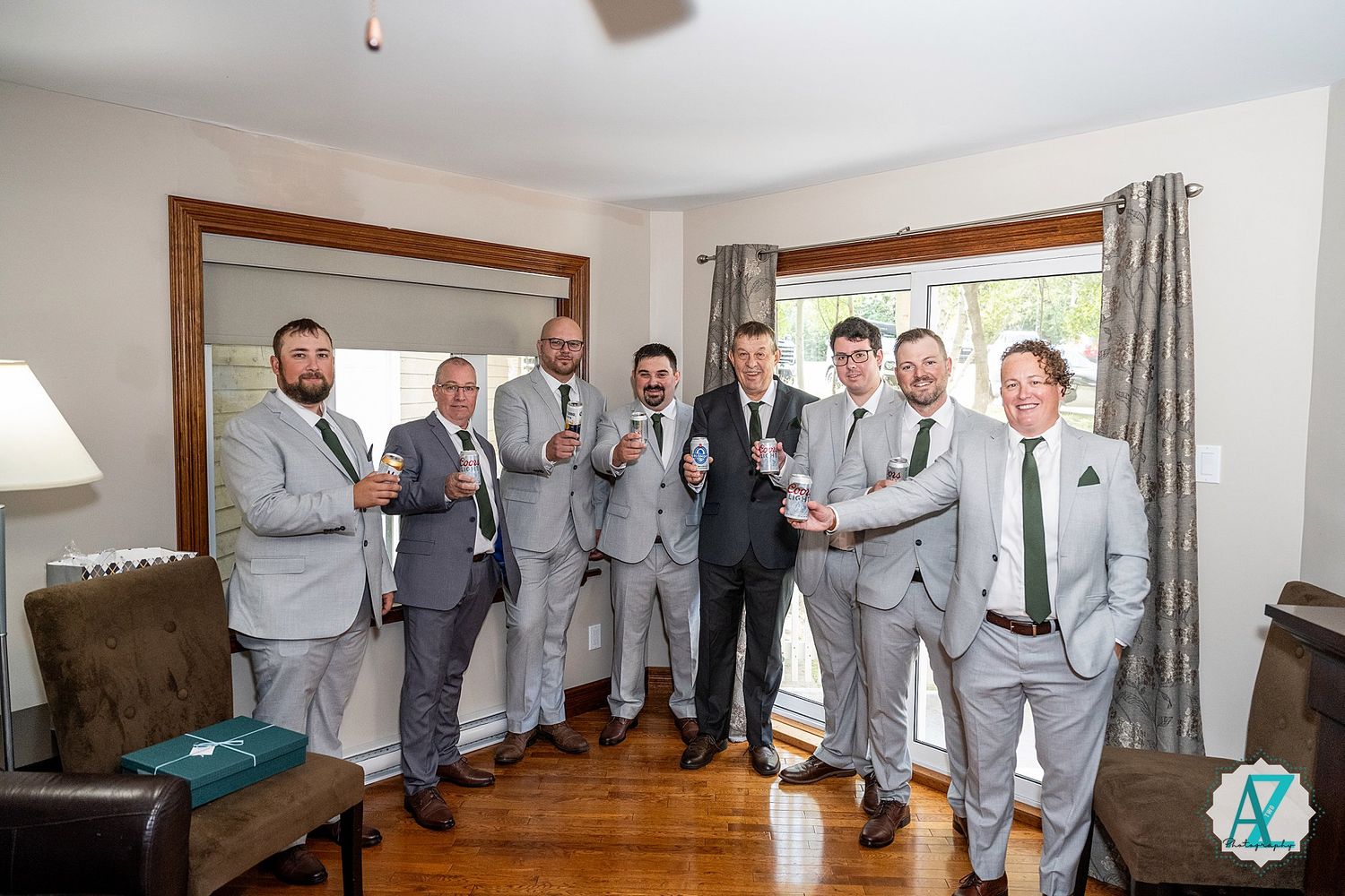 Groomsmen in light gray suits gather around in preparation for a wedding day celebration.