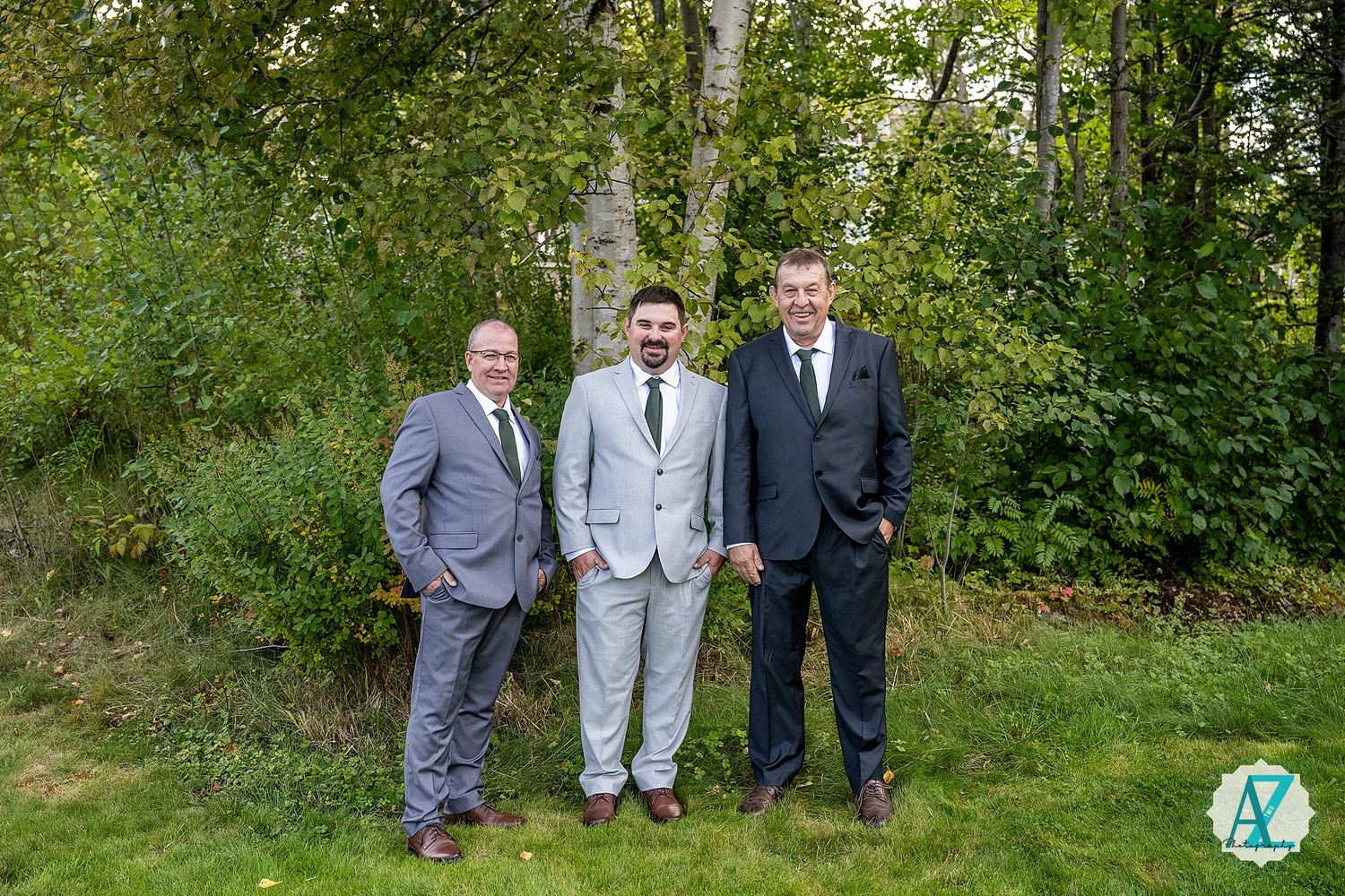 A group poses together in formal attire against a lush green outdoor background.