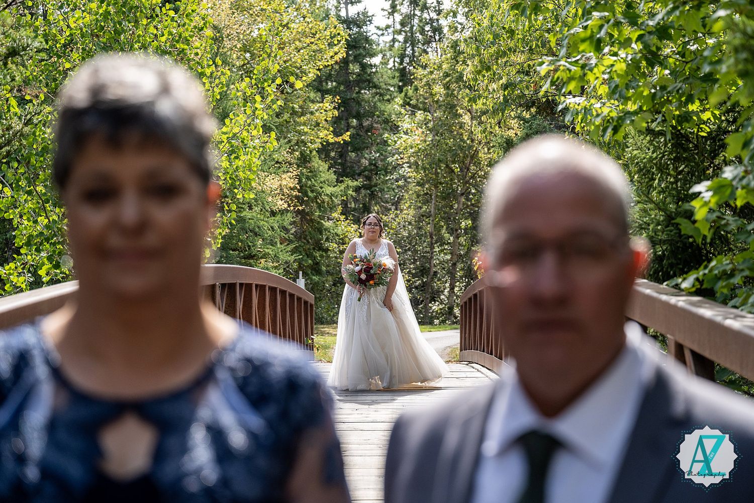 Wedding party members gather on a wooden bridge surrounded by green foliage.