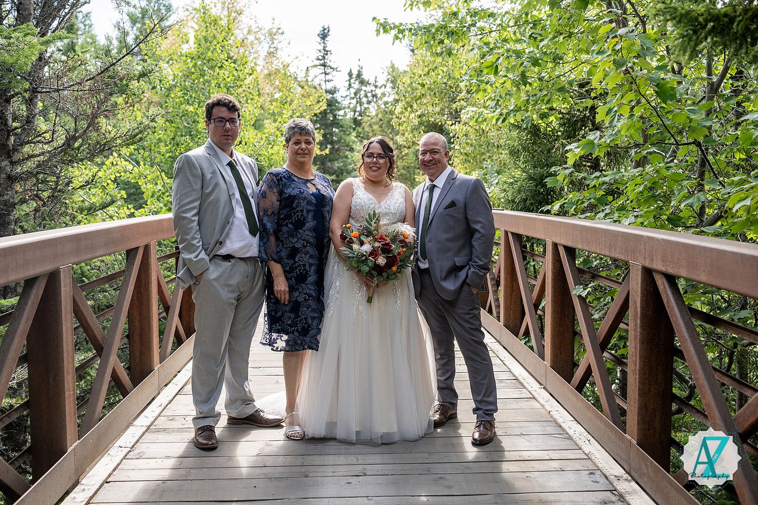 Wedding party standing on a rustic wooden bridge surrounded by green foliage.