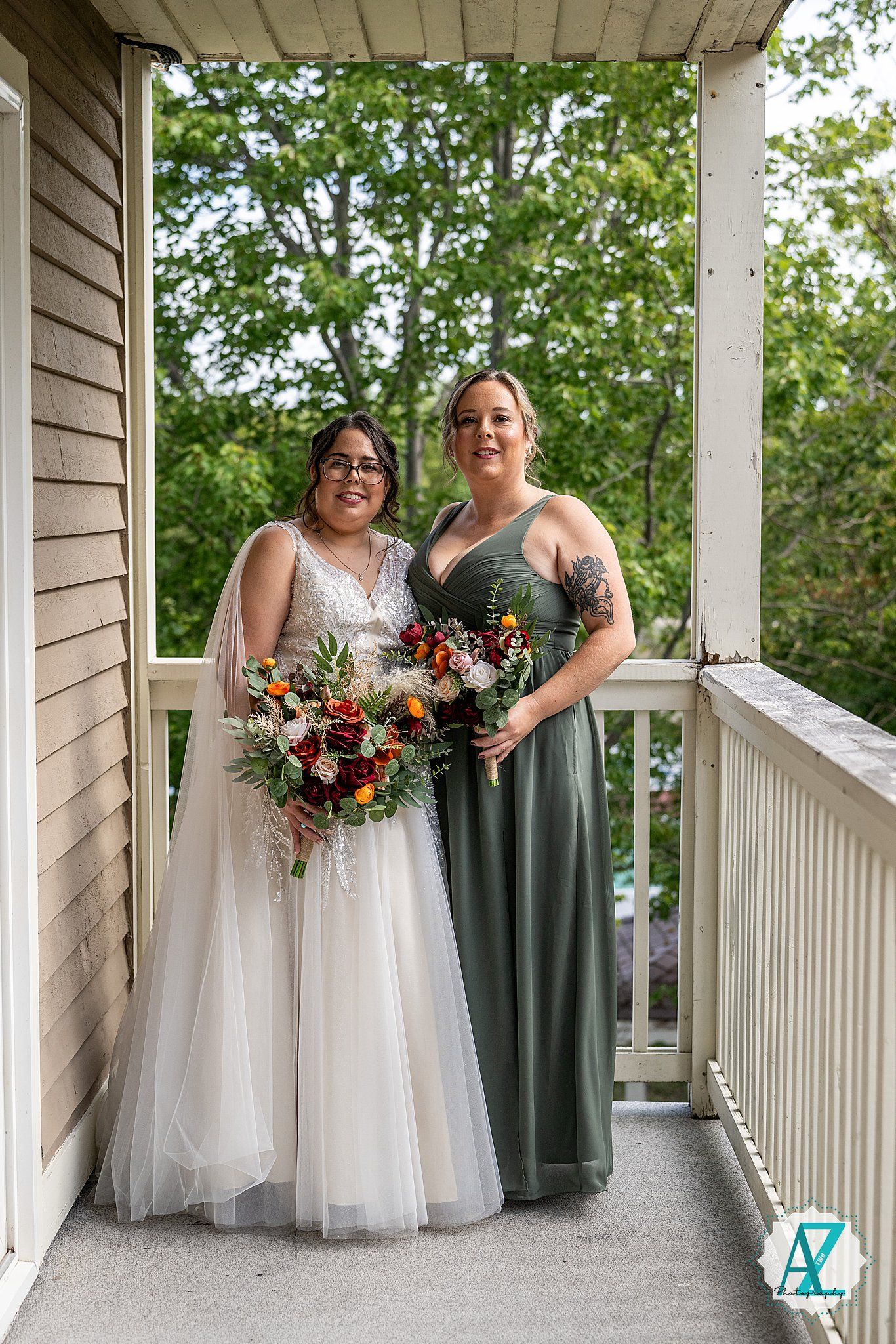 Wedding party members in white and sage green dresses pose together on a sunlit wraparound porch.