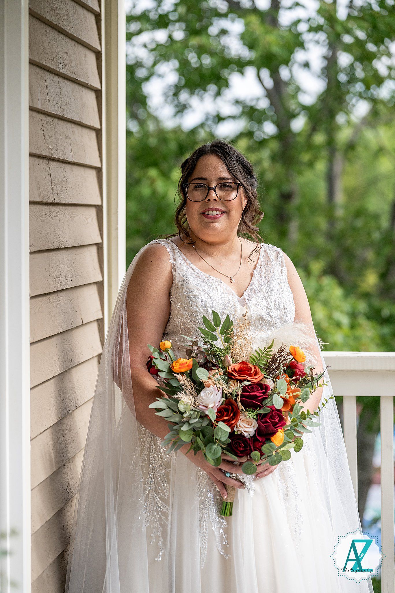 Two people in white wedding dresses hold vibrant autumn-colored bouquets on a covered porch.