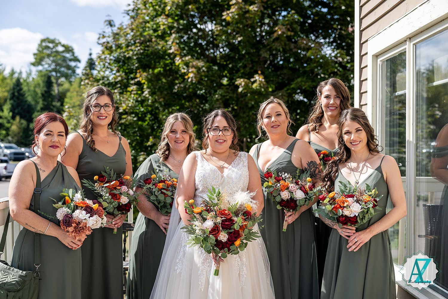 Wedding party members in grey dresses pose with colorful floral bouquets outdoors.