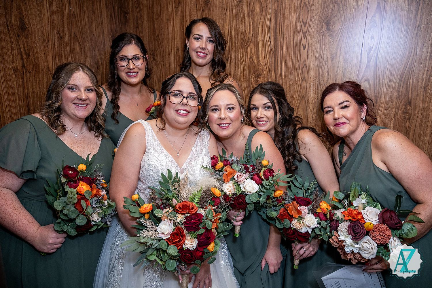 Bridal party in forest green dresses poses with vibrant autumn-colored bouquets.