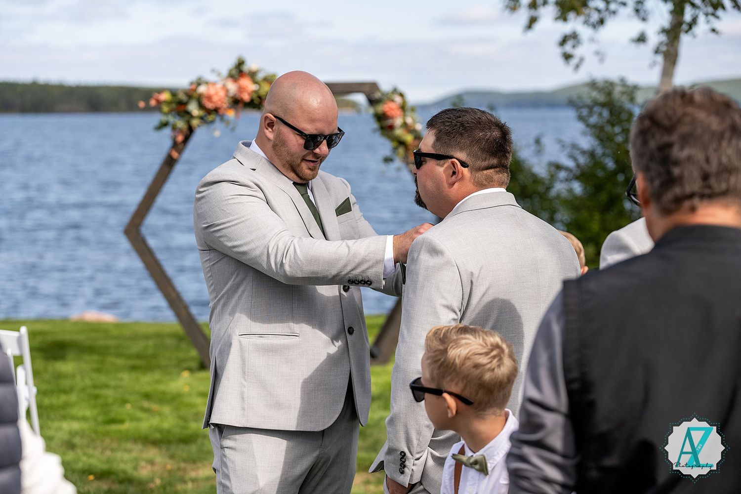 Two people share an emotional moment at a waterfront ceremony with other guests looking on under sunny skies.