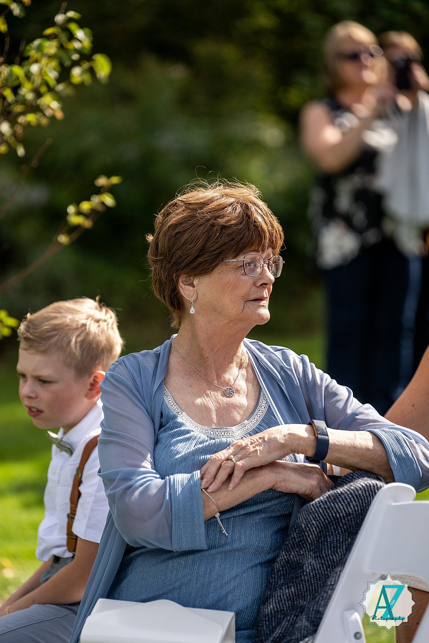 A touching moment during an outdoor wedding ceremony as attendees sit in white chairs on the grass.