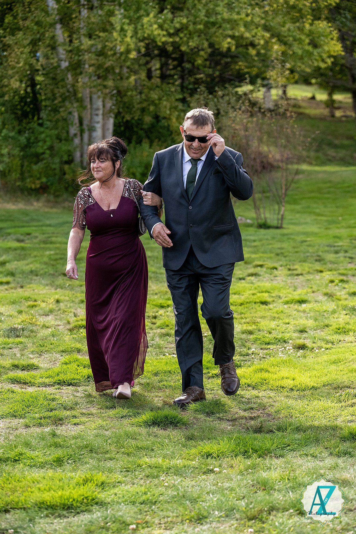 Two people in formal attire cautiously walk through a sunlit grassy field during an outdoor event.