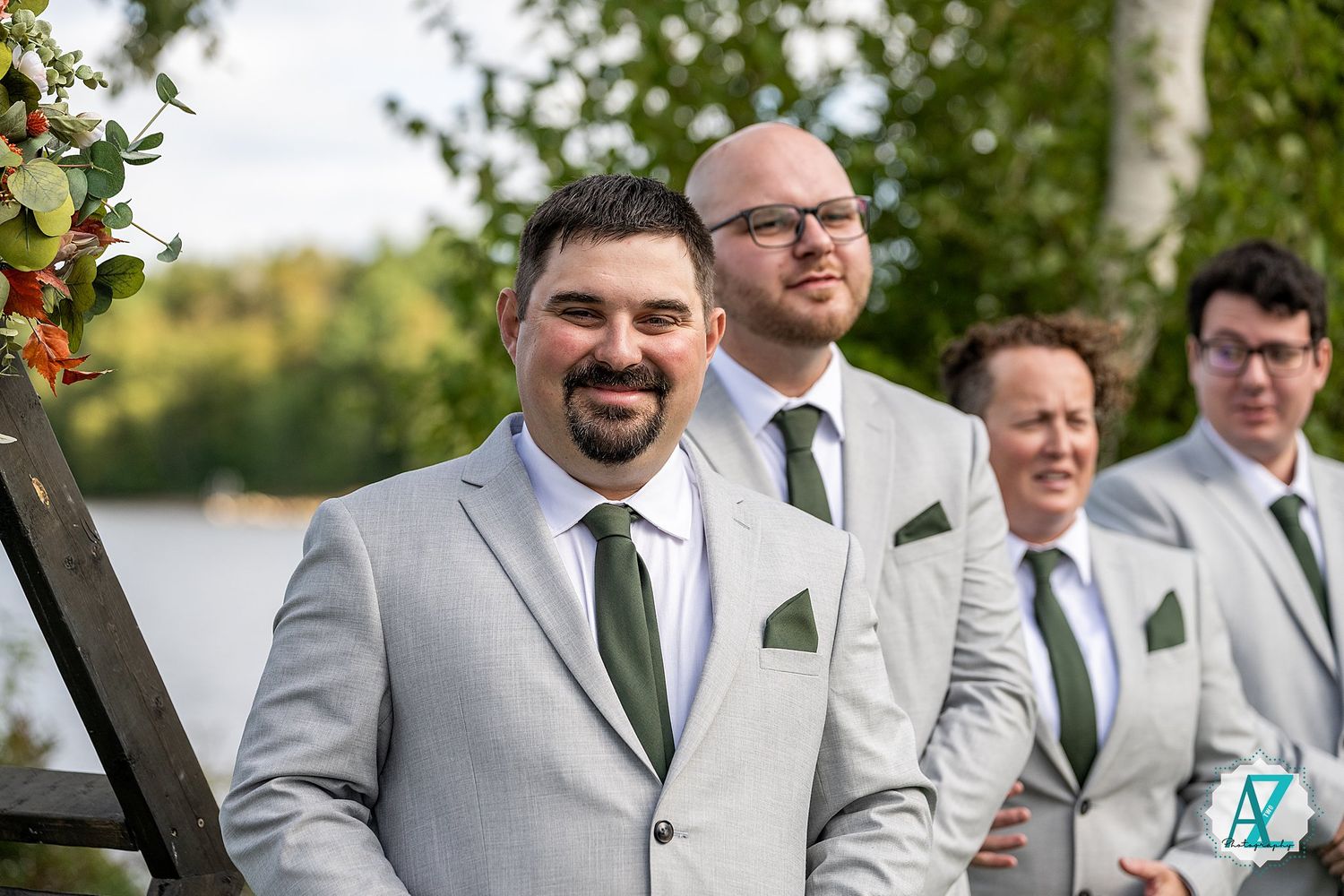 Groomsmen in light gray suits with green ties pose together at an outdoor wedding venue.